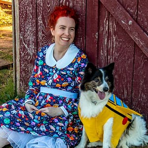 Brianna, dressed as Ms Frizzle with a space-themed dress and bright red hair, sitting next to Beau, a black and white border collie mix dressed as the Magic School Bus